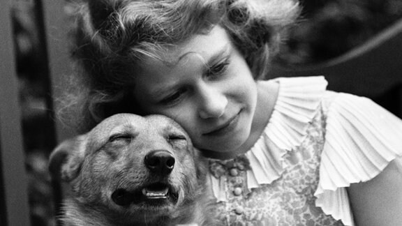 Queen Elizabeth als junges Mädchen kuschelt sich an einen Hund.