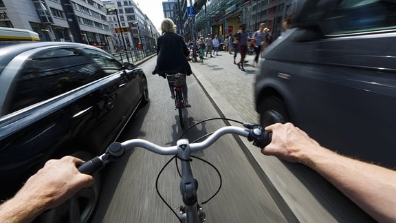Ein Radfahrer wird im Stadtverkehr von einem nah vorbeifahrenden Auto überholt
