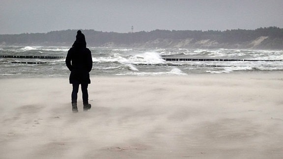 Eine Frau geht an einem stürmischen Strand spazieren