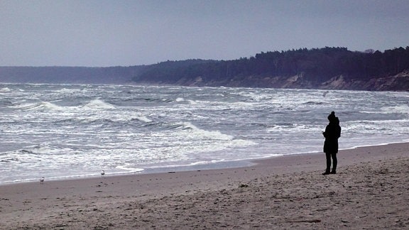 Eine Frau geht an einem stürmischen Strand spazieren
