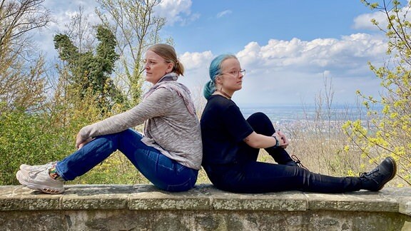 Zwei Frauen sitzen auf einer Steinmauer.