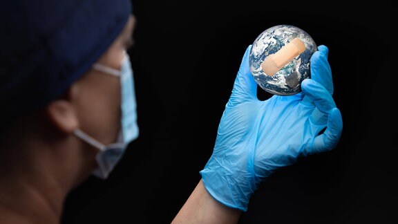 Arzt mit Gesichtsmaske und chirurgischen Handschuhen hält bandagierten Planeten Erde