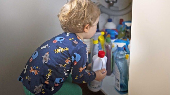 Ein Junge schaut in den Schrank mit Putzmitteln