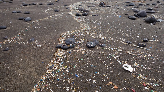 Angespühltes Mikroplastik auf dunklem Lavasand