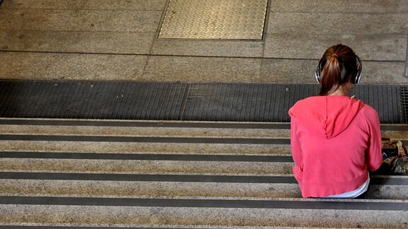 Ein Kind mit Kopfhörern sitzt einsam auf Stufen an der U-Bahn