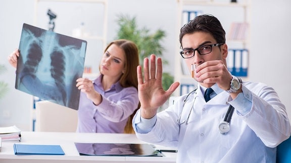 Symbolfoto: Eine Frau hält ein Röntgenbild und ein Mann zeigt eine zerbrochene Zigarette