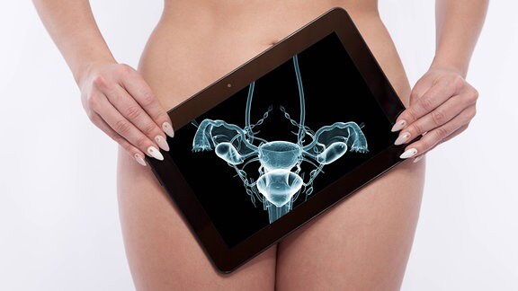 Eine nackte Frau hält ein Tablet auf dem der Unterleib als Röngenaufnahme zu sehen ist