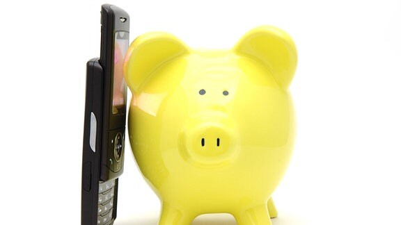 Ein Telefon lehnt an einem gelben Sparschwein.