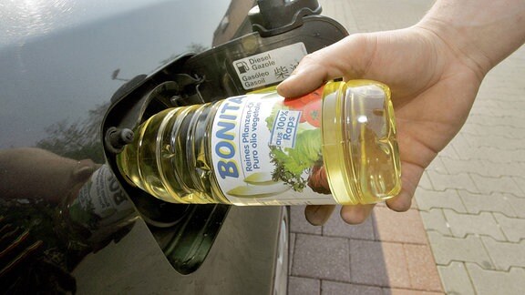 Mann befüllt den Tank seines Autos mit Pflanzenöl aus Raps