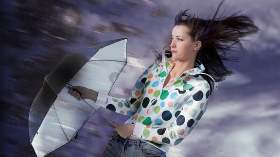 Junge Frau hält Regenschirm gegen den Wind