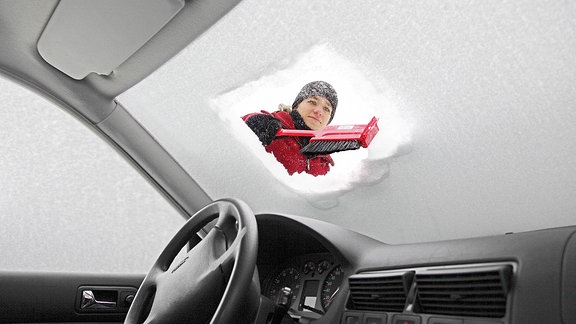 Frau entfernt im Winter Schnee und Eis von der Windschutzscheibe eines tief eingeschneiten Autos. 