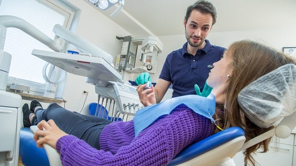 Ein Zahnarzt gibt einer Patientin in einer Zahnarztpraxis einen Anti-Stress-Wuerfel zur Beruhigung in die Hand (gestellte Szene).