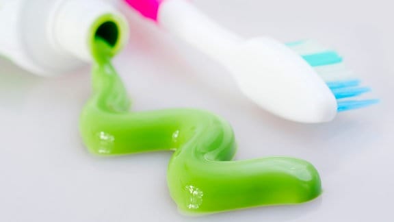 Zahnbürste liegt neben Zahnpastatube, aus der grüne Zahnpasta läuft.
