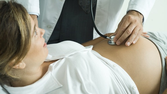 Ein Arzt hört einer schwangeren Frau den Bauch mit einem Stethoskop ab.