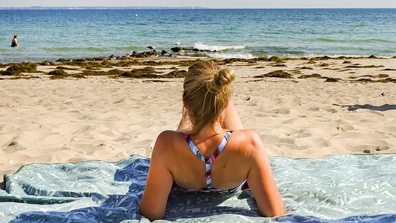 Eine Urlauberin genießt das sommerliche Wetter am Ostseeufer in Timmendorfer Strand.