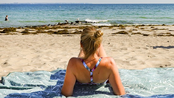 Eine Urlauberin genießt das sommerliche Wetter am Ostseeufer in Timmendorfer Strand.