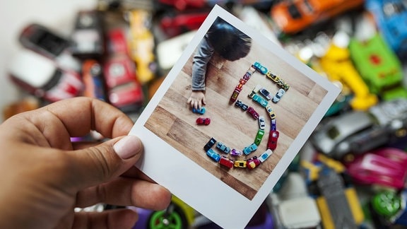 Polaroid von einem kleinen Kind und Spielzeugautos, die zur Zahl Fünf angeordnet wurden