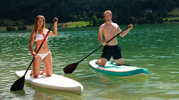 Pärchen beim Stand-Up Paddeln, kniend auf den Boards