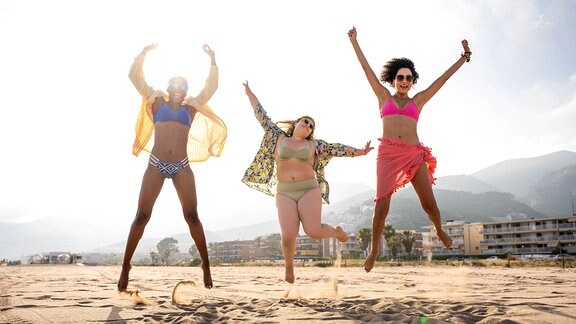 Drei Frauen springen am Strand in die Luft.