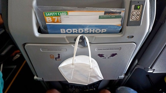 Eine FFP2-Maske hängt an der Lehne eines Passagier-Flugzeuges.