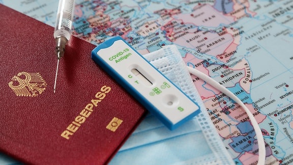 Reisepass, Schutzmaske, Schnelltest und Spritze auf einer Landkarte