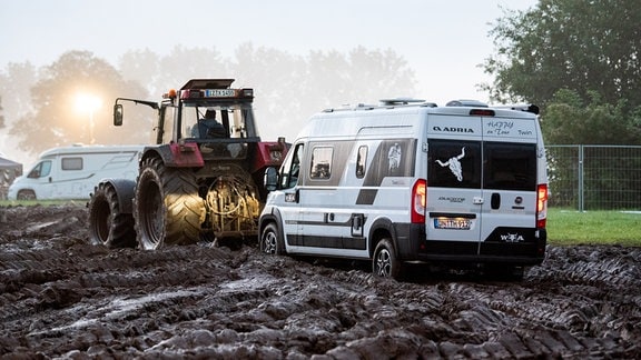 Ein Fahrzeug wird mit Hilfe eines Traktors auf das Gelände des Heavy-Metal-Festivals in Wacken durch den Schlamm gezogen