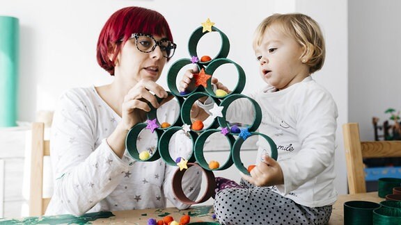 Mutter und Tochter beim Basteln zu Hause mit Zubehör, um ein Weihnachtsbaum zu machen.