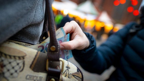 Eine Hand zieht Geldscheine aus einer Handtasche. 