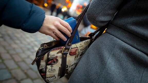 Eine Hand zieht ein Portemonnaie aus einer Handtasche.