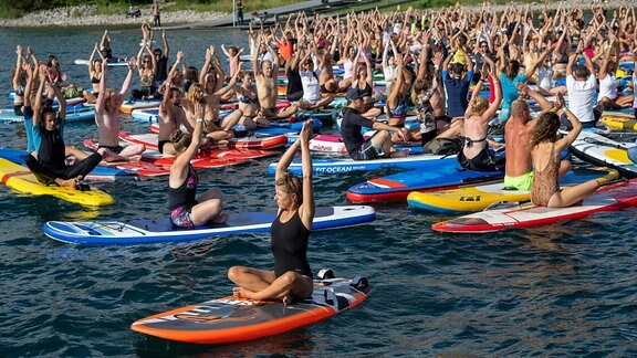 Bei einer Yogastunde auf einem See absolvieren die Teilnehmer ihre Übung auf Stand-up-Paddles