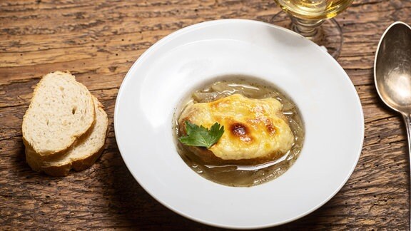 Baguettescheiben, Löffel und Glas neben einem Teller Französischer Zwiebelsuppe 