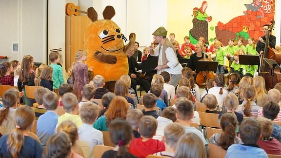 Die Maus aus der "Sendung mit der Maus" steht mit MDR-Musikvermittler Ekkehard Vogler im Kostüm auf der Bühne eines MDR-Clara-Schulkonzerts in Radeburg.