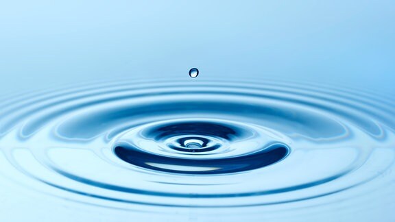 Ein Wassertropfen zieht Kreise auf einer blauen Wasseroberfläche.