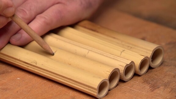 Mit einem Bleistift werden Markierungen auf kleine Bambusröhrchen gezeichnet.