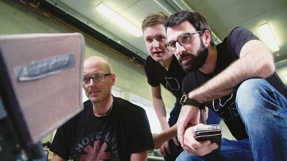 Drei Männer sehen auf einen Monitor