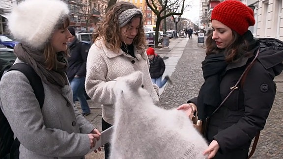 Drei Frauen stehen beieinander und betrachtn ein Stück Stoff.