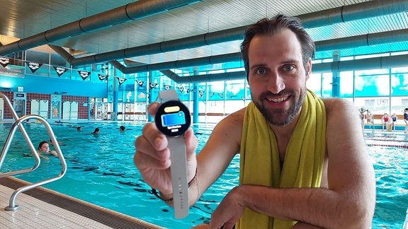 Mann im Schwimmbad hält Armbanduhr in die Kamera.