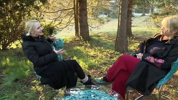 Zwei Frauen sitzen im Garten auf Stühlen und führen ein Gespräch.
