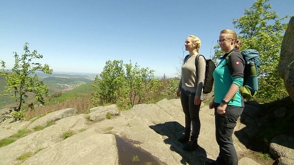 Zwei Frau stehen an einem Aussichtspunkt auf einem Berg und bewundern die Aussicht.