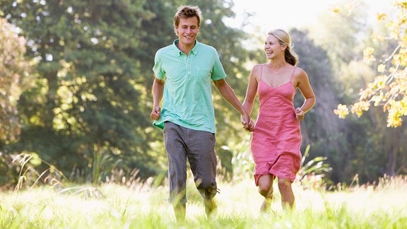 Ein junges Paar läuft durch einen sonnigen Laubwald.