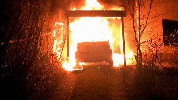 Ein Auto brennt nachts in einer Einfahrt.