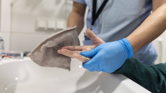 Eine Pflegerin wäscht die Hand eines älteren Mannes