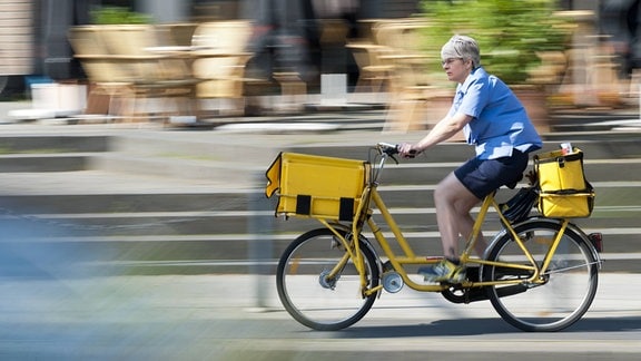 Eine Briefträgerin fährt mit dem Fahrrad durch die Stadt