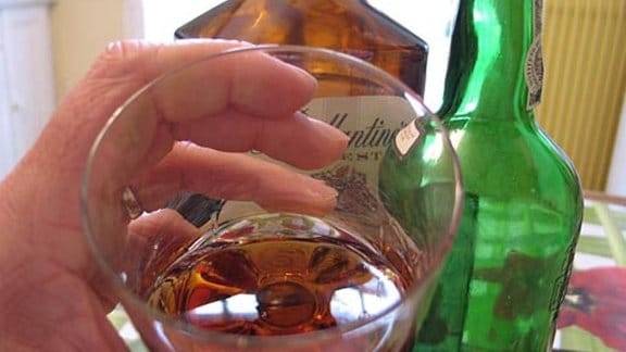 Ein mit einer braunen Flüssigkeit gefülltes Glas und 2 leere Schnapsflaschen.