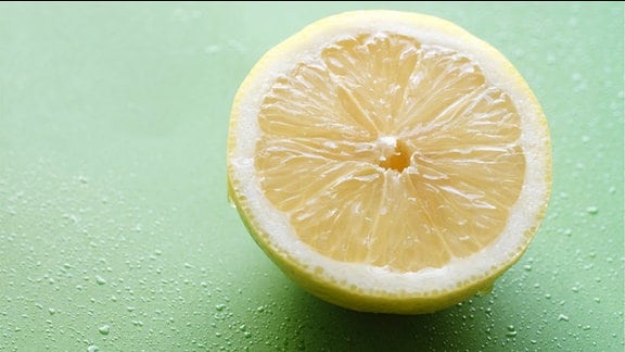 Eine Zitronenhälfte im Anschnitt vor grünem Hintergrund.