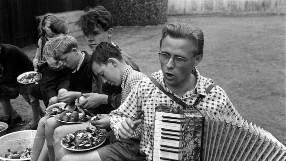DDR 1950 - Akkordeonspieler unterhält Jungs beim Kartoffelschälen