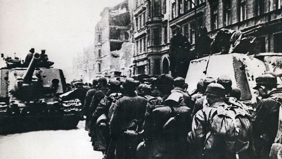 Deutsche Soldaten passieren auf dem Weg in die Gefangenschaft einen russischen Panzer.