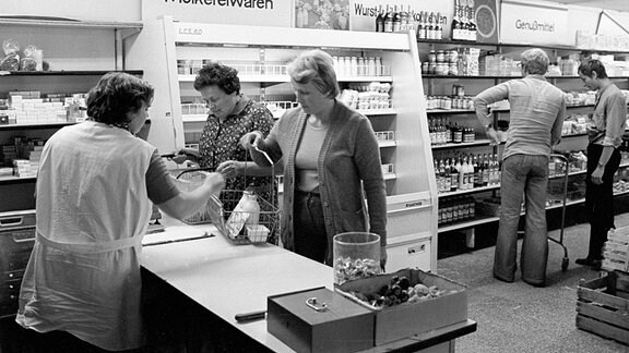 Eine Kundin steht im Konsum an der Kasse und unterhält sich mit der Kassiererin, DDR 1981