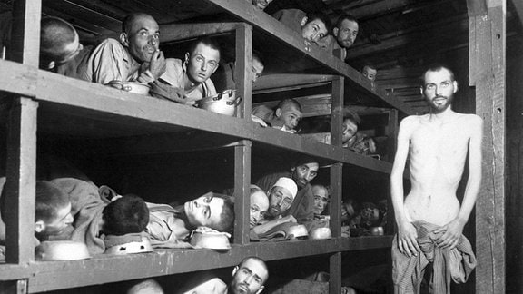 Innenansicht einer Häftlingsbaracke in Buchenwald: Mehrere Menschen liegen in einem Holzgestellt.