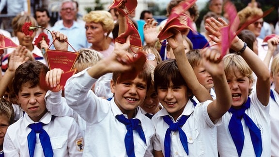 Jungpioniere in traditioneller Kleidung mit weißem Hemd und blauem Halstuch schwenken Wimpel auf denen "25 Jahre antifaschistischer Schutzwall" steht, aufgenommen bei einer Pionier-Demonstration am 13.08.1986 in Ost-Berlin anlässlich einer SED-Kundgebung zum 25. Jahrestag des Mauerbaus.